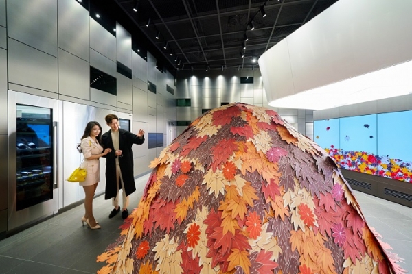 LG전자가 유명 아티스트 '나난'과 협업해 프리미엄 빌트인 가전 브랜드 '시그니처 키친 스위트(SIGNATURE KITCHEN SUITE)' 논현 쇼룸에서 이달 27일까지 특별 전시회를 연다. 모델들이 시그니처 키친 스위트 컬럼형 와인셀러(사진 왼쪽), LG 올레드 비디오월 사이니지(사진 오른쪽)가 전시된 논현 쇼룸 1층 라운지에서 낙엽 오브제를 쌓아 만든 나난의 작품을 감상하고 있다. (사진=LG전자)